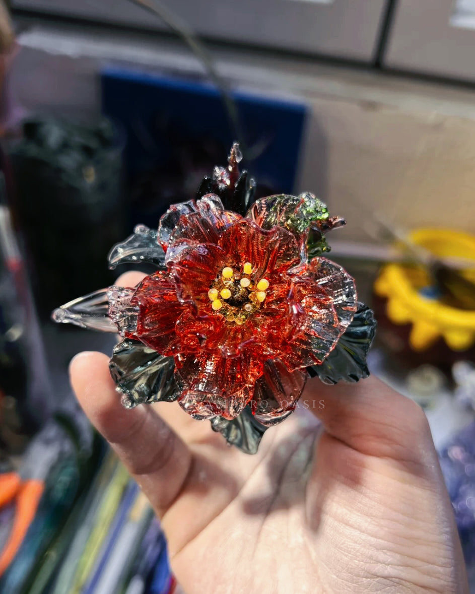 An artisan using traditional lampworking techniques, melting and shaping glass over a torch flame to create the camellia incense holder.