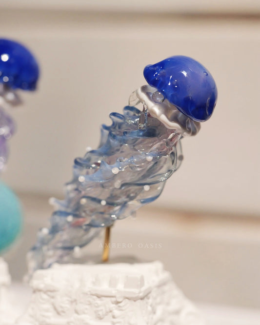 Ocean Blue Series hand-blown glass jellyfish blind box by Ambero Oasis, featuring a vibrant deep blue cap and clear twisted tentacles.