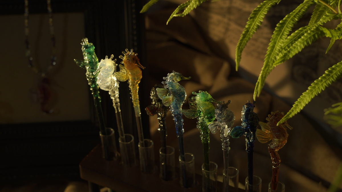  handmade lampwork glass seahorse drink stirrers, magical talisman barware, 18cm long, crossed display on dark background with botanical border.